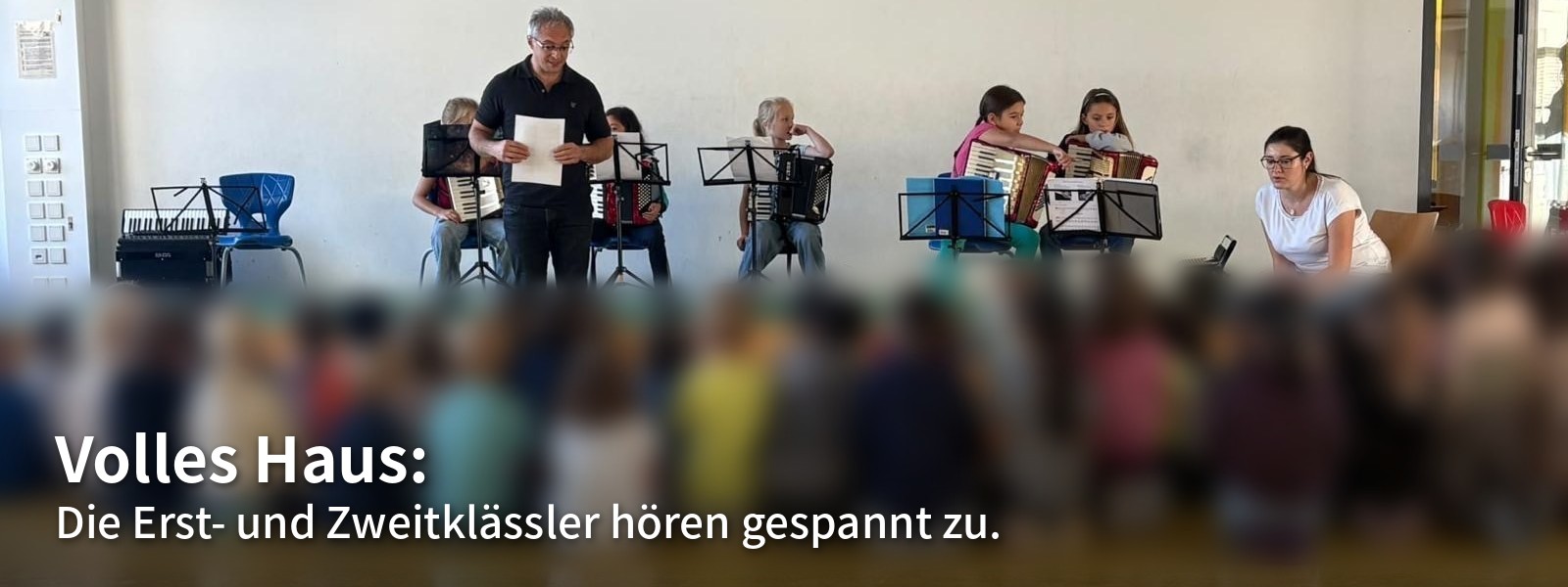Volles Haus: Die Erst- und Zweitklässler hören gespannt zu. Viele Kinder sitzen vor der Bühne beim Akkordeon-Vorspiel.