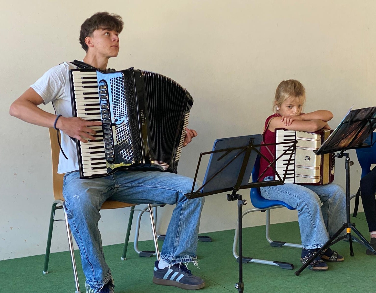 Ein Jugendlicher mit großem Akkordeon neben einer jungen Spielerin